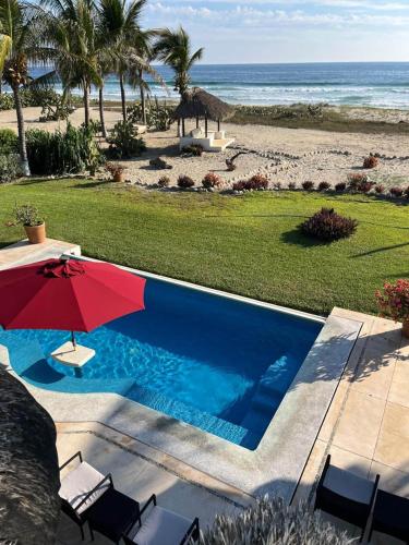 a swimming pool with a red umbrella and the beach at Casa Fuente Ocean Villa in Santa María Colotepec