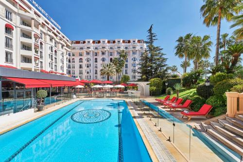 a swimming pool with chairs and a building at Hôtel Barrière Le Majestic Cannes in Cannes