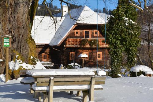 een houten huis in de sneeuw met een bank voor bij Zehna Hube in Semriach