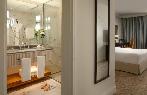 a bathroom with a bed a sink and a mirror at Corinthia St George's Bay in St. Julianʼs