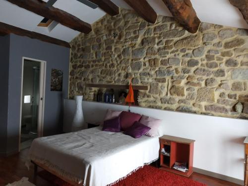 a bedroom with a stone wall and a bed with purple pillows at Village house 8 beds in Joncels