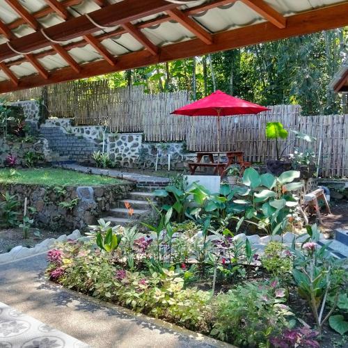 a garden with a red umbrella and some plants at Gecko Lodge in Tetebatu
