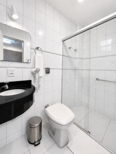 a white bathroom with a toilet and a sink at Hotel Castelo in Gravatal