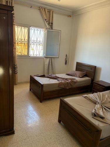 two beds in a room with two windows at Résidence El hechene in Ḩawmat al Ḩashshān
