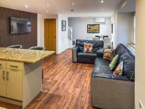 a living room with a black leather couch and a kitchen at Roslyn Cottage in Hamsterley
