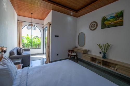 a bedroom with a bed and a chair and a window at Juna Guest House in Uluwatu