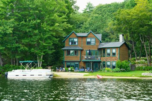ein großes Haus am Wasser mit einem Boot davor in der Unterkunft Casco Cottage in Casco