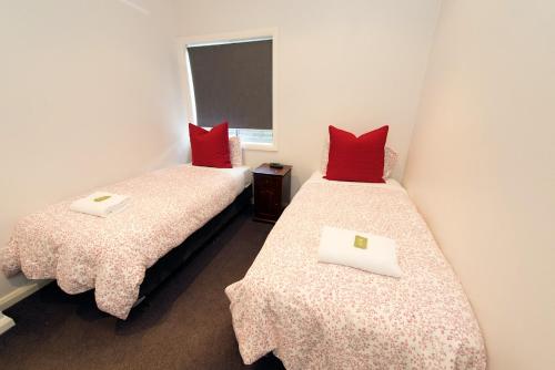 two twin beds in a room with red pillows at Apartments by Townhouse in Wagga Wagga