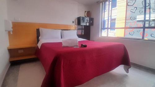 a bedroom with a bed with a red blanket and a window at Hotel Bonaire Un Estilo Difrente in Bogotá