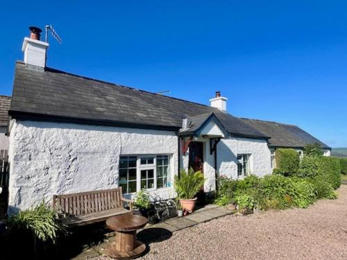 a white building with a bench in front of it at Tornaroan Cottage in Ballycastle