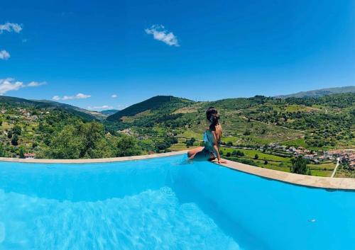 a woman sitting on the edge of a swimming pool at Private Douro- Quinta das Susandas in Mesão Frio