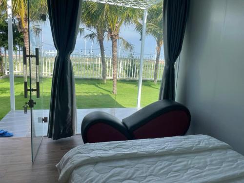 a bedroom with a bed and a window with palm trees at homestay windhills in Ấp Nhơn Hòa