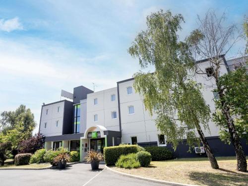 a large white building with a parking lot at Ibis Styles Cognac in Châteaubernard