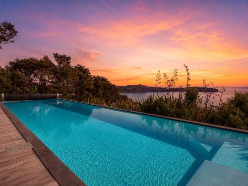 a swimming pool with a sunset in the background at No 63 - Stay Waiheke in Onetangi