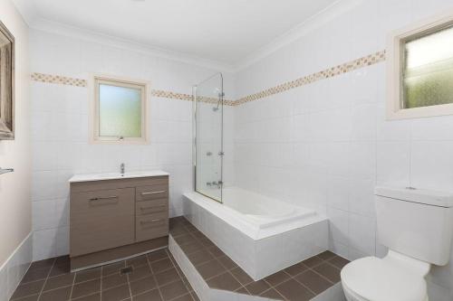 a white bathroom with a tub and a toilet and a sink at Rock On Cottage in Jindabyne