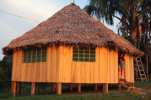 a small hut with a thatched roof and a person standing on a ladder at Hostal Maguare-Reserva Indígena Maguare in Leticia