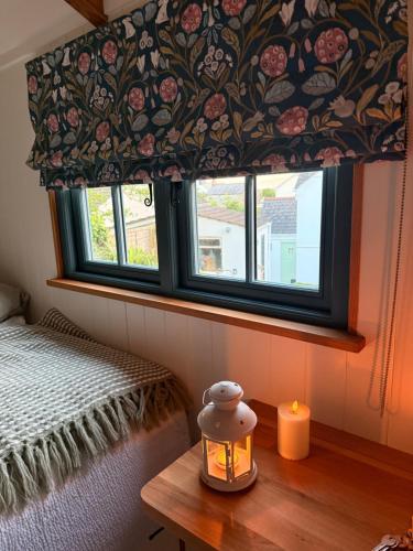 a window with a flower patterned curtain and a candle at Shepherds Hut in St Austell
