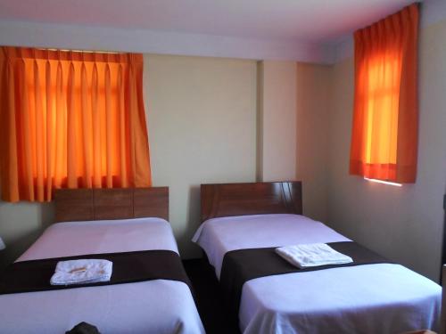 two beds in a room with orange curtains at Hostal Casa del Montañista in Huaraz