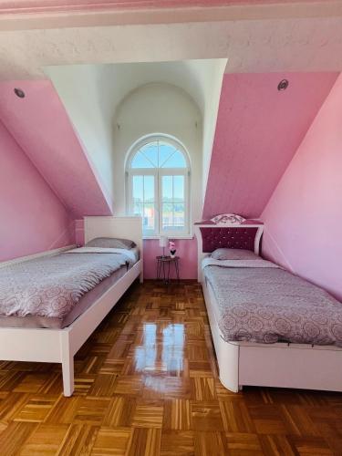 two beds in a room with pink walls and wooden floors at Vila Natalija in Ljubljana
