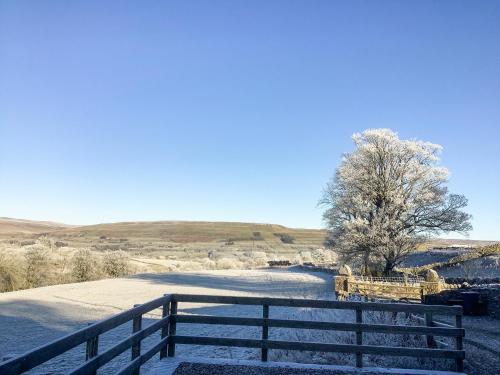 a fence and a tree in a snowy field at Aysgill Cottage in Hawes
