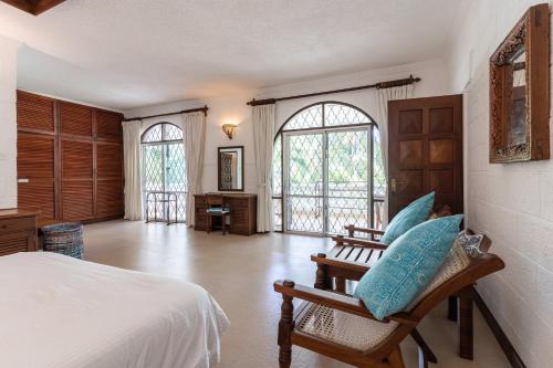 a bedroom with a bed and chairs and windows at Watano Beach House Diani in Diani Beach