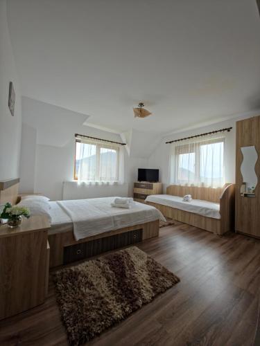 two beds in a room with wooden floors and windows at Popasul Găleșean in Galeşu