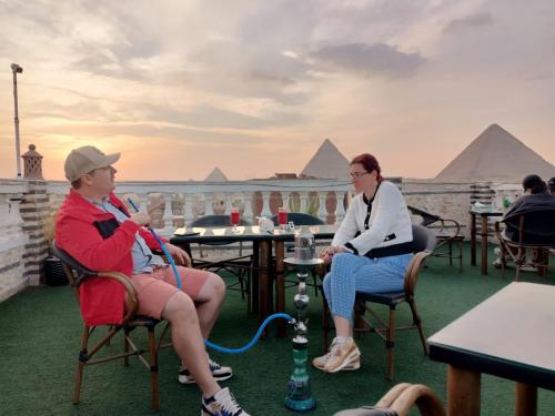two women sitting in chairs on a roof with pyramids in the background at Magic pyramids star hotel in Cairo