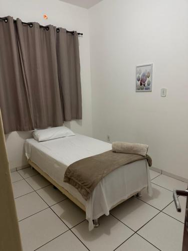 a bed in a white room with a window at Ap 07 mazzonetto in Primavera do Leste