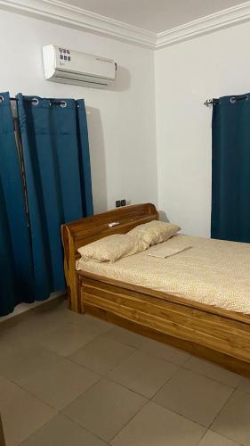 a bedroom with a bed and blue curtains at New ACROPOLE in Komé