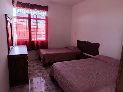 a room with two beds and a window with red curtains at DEPARTAMENTOS AMUEBLADOS CELIA in Morelia
