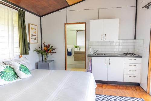 a bedroom with a white bed and a kitchen at Ariki Retreat - Adults Only in Rarotonga