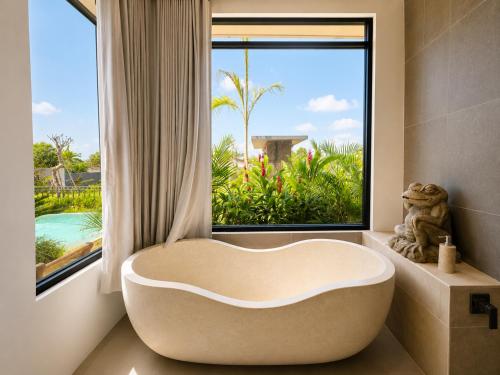 a bath tub in a bathroom with a large window at KAPI Sebatu Villa in Tampaksiring