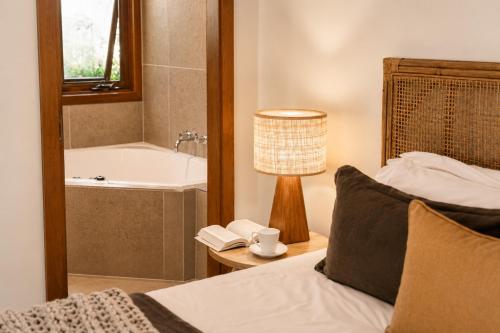 a bedroom with a bed and a bath tub and a lamp at Cape Byron Retreat (Adults-Only) in Byron Bay