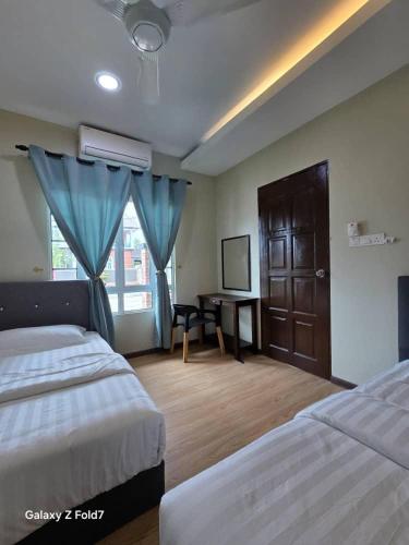 a bedroom with two beds and a desk with a window at PJ Luxury Homestay in Sipitang