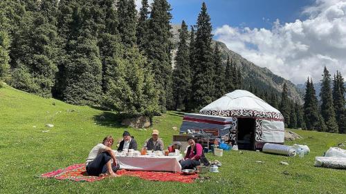 a group of people sitting around a table in a field at Kapchygai Yurt Camp in Dzhetyoguz