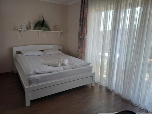 a bed with white sheets and pillows in a room with windows at Napolá apartman in Balatonalmádi