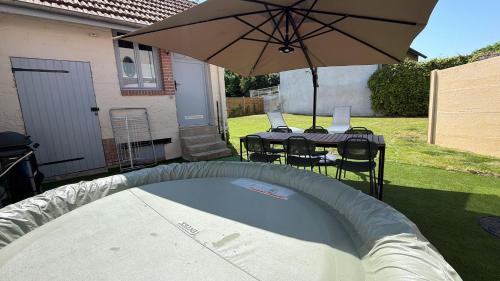 a backyard with two tables and an umbrella at Maison Cosy, proche Reims, La Nichée in Bazancourt