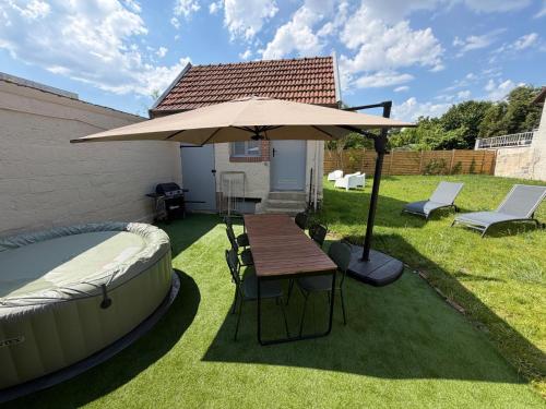 a table with an umbrella next to a hot tub at Maison Cosy, proche Reims, La Nichée in Bazancourt