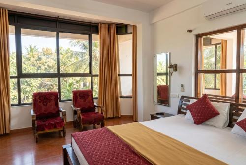 a bedroom with a bed and two chairs and windows at Samudra heritage in Cochin