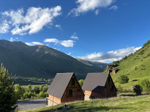 two barns on a hill with mountains in the background at Gagma Chalets Kazbegi in Kazbegi