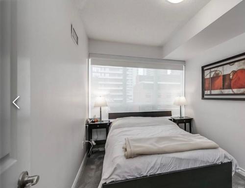 a white bedroom with a bed and two tables with lamps at Urban Nest in Toronto