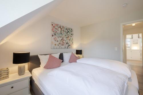 a bedroom with a bed with white sheets and pink pillows at Strandliebe Sylt in Westerland