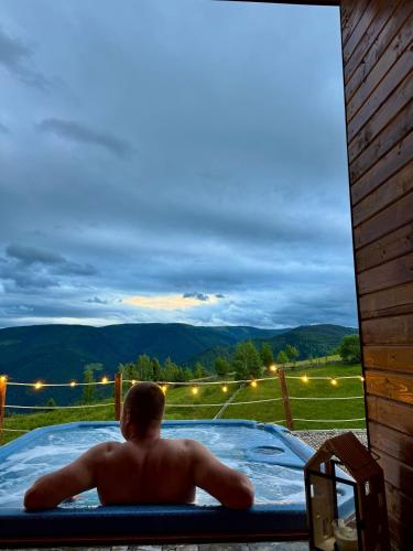 a man laying in a hot tub with a view at Old Man's Cabin in Măguri