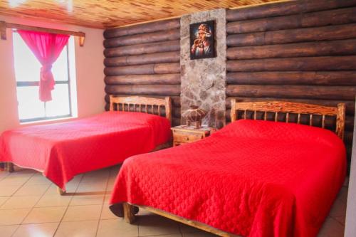 two beds in a room with red sheets at Cabañas sierra grande in Creel
