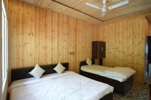 two beds in a room with wooden walls at The Great Hill View Hotel in Phata