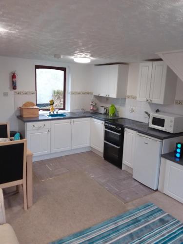 a kitchen with white cabinets and black appliances at Sandy Toes Cottage in Penzance