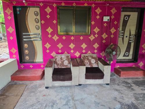 two chairs sitting in front of a pink house at Pilankar Guest House in Ratnagiri
