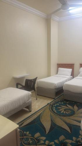 a room with two beds and a chair and a rug at فندق منازل الراشدين in Az Zahrāʼ