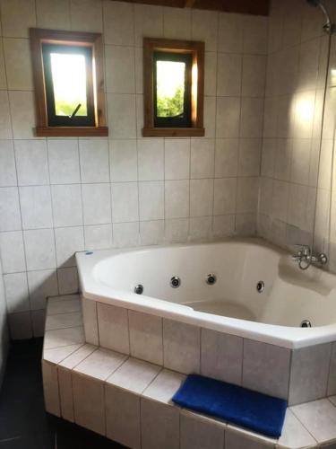 a large white tub in a bathroom with two windows at Cabañas Loncoche Puerta del Sol in Loncoche