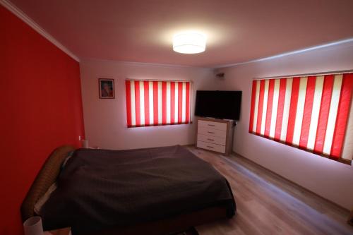 a bedroom with red curtains and a bed and a television at Kicsipatak vendégház in Lunca de Sus